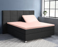 Roze satijnen splittopper hoeslaken op een boxspring met donkergrijs hoofdbord, één hoofdeinde omhoog gezet