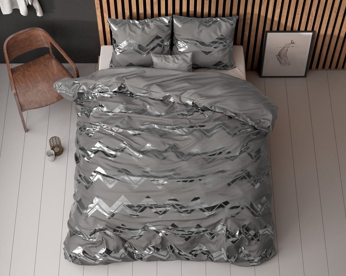 Grijs dekbedovertrek met zilverkleurig glanzend zigzagdessin en bijpassende kussenslopen op een bed, gezien van boven