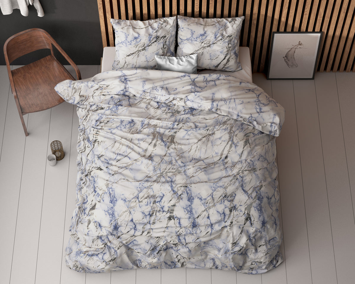 Dekbedovertrek met blauw-grijs marmerprint op een bed met kussens, gezien van boven, naast een houten stoel