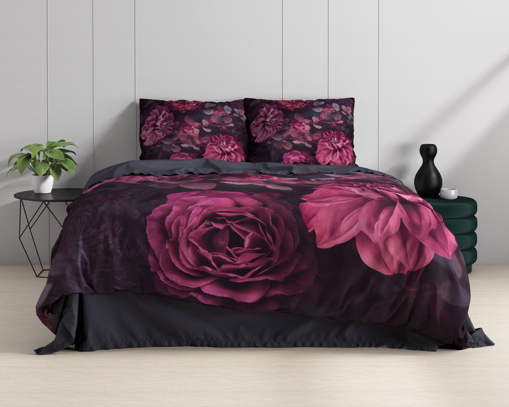 Opgemaakt bed met dekbedovertrek met grote rode rozen en bloemen op donkere ondergrond, naast plant en zij-tafeltjes