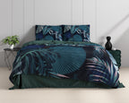 Bed met blauw dekbedovertrek met botanische bladprint en effen groene achterzijde, naast een plant en groene poef