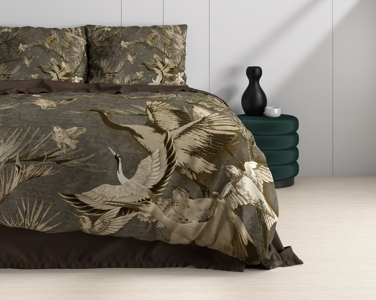 Bed met taupe dekbedovertrek met print van kraanvogels en palmbladeren, naast een groen nachtkastje met zwarte vaas