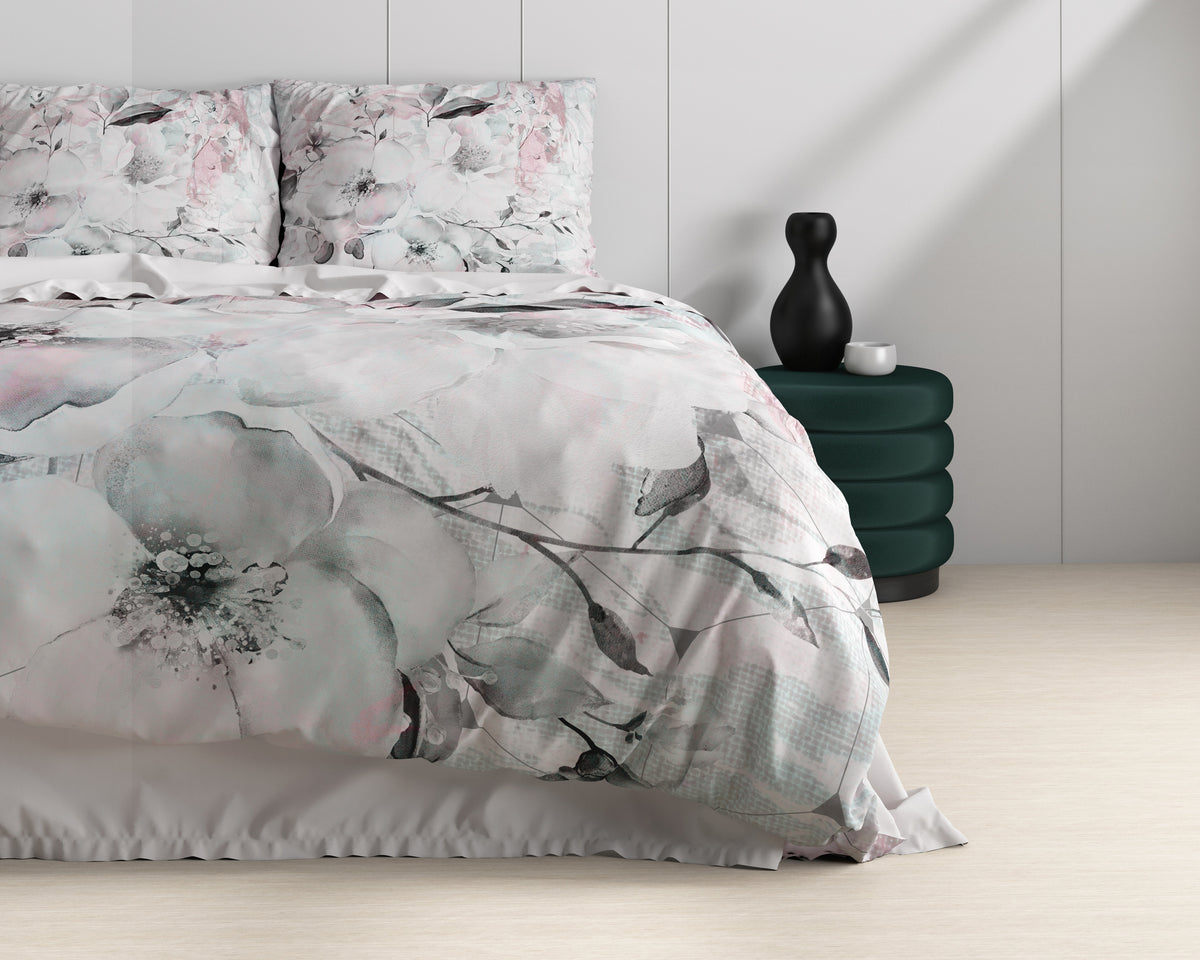 Bed met dekbedovertrek met grote bloemenprint in wit, roze en grijsgroen, naast een groen fluwelen poefje met zwarte vaas