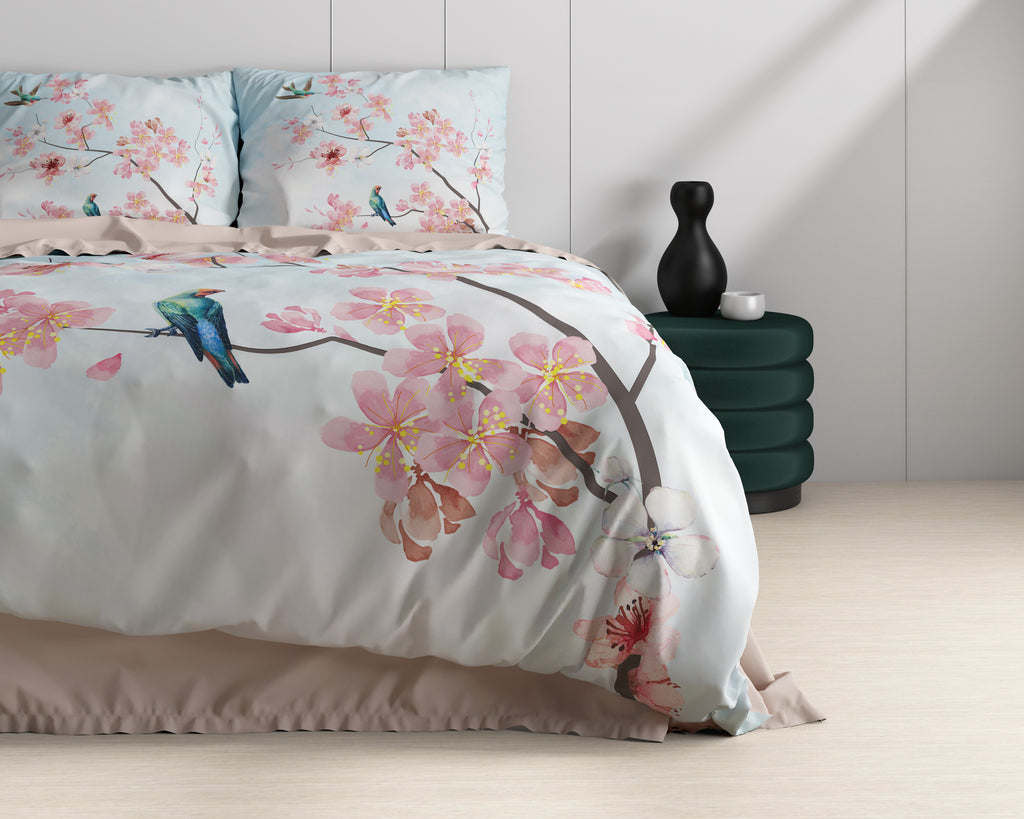 Bed met blauw dekbedovertrek met roze bloesems en een vogel, naast een donkergroene poef met zwarte vaas