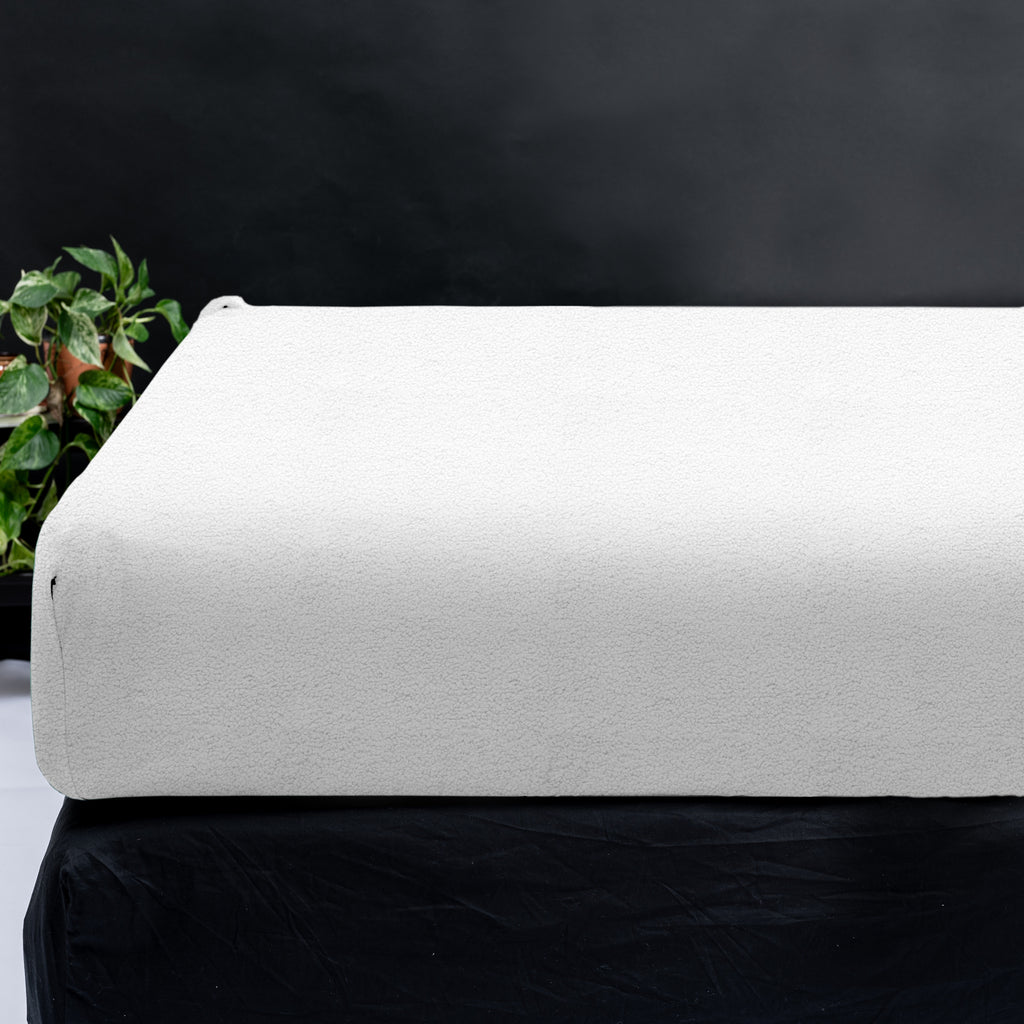 Wit teddy hoeslaken om een matras op een zwarte ondergrond, met een plant links