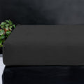 Antraciet teddy hoeslaken om een matras, met een plant op de achtergrond