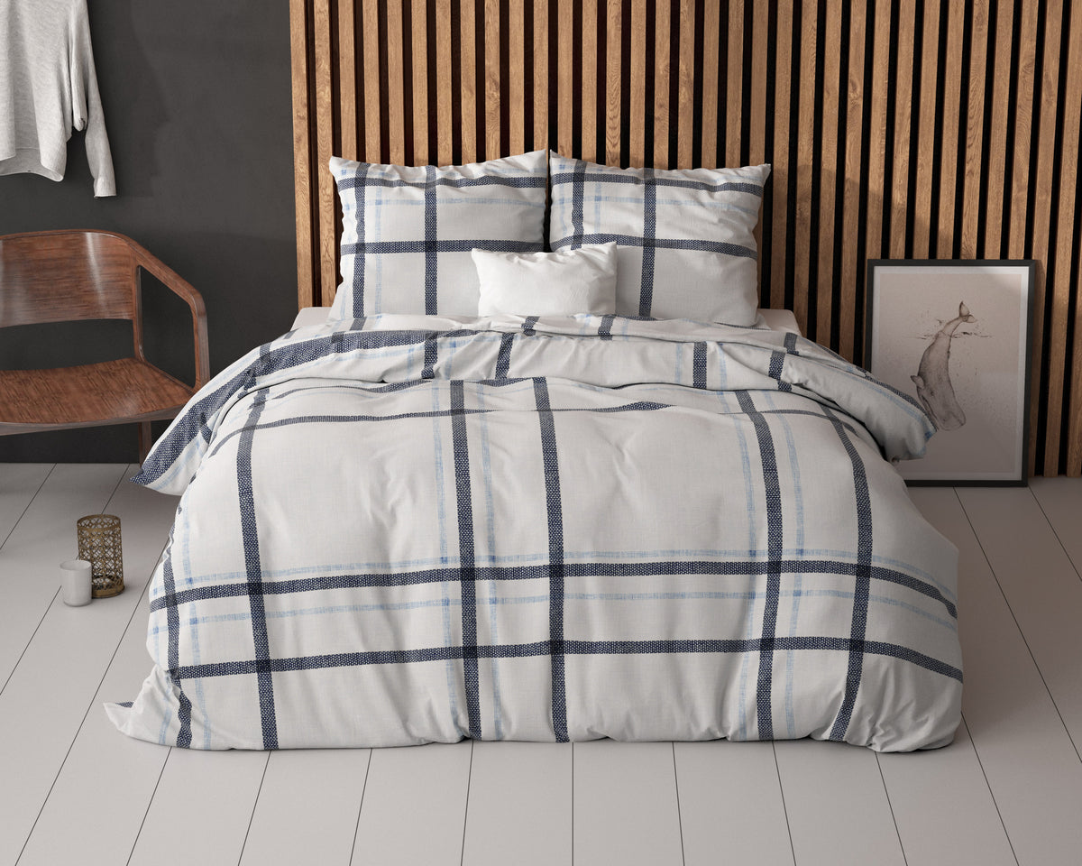 Bed met wit dekbedovertrek met blauw ruitpatroon en twee kussens voor een houten lamellenwand