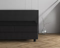 Donkere topper op een grijs boxspringbed met hoofdbord, naast een glazen vaas met tak op een visgraatvloer