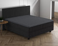 Antracietkleurig hoeslaken over een topper op een donkere boxspring met hoofdbord in een lichte slaapkamer