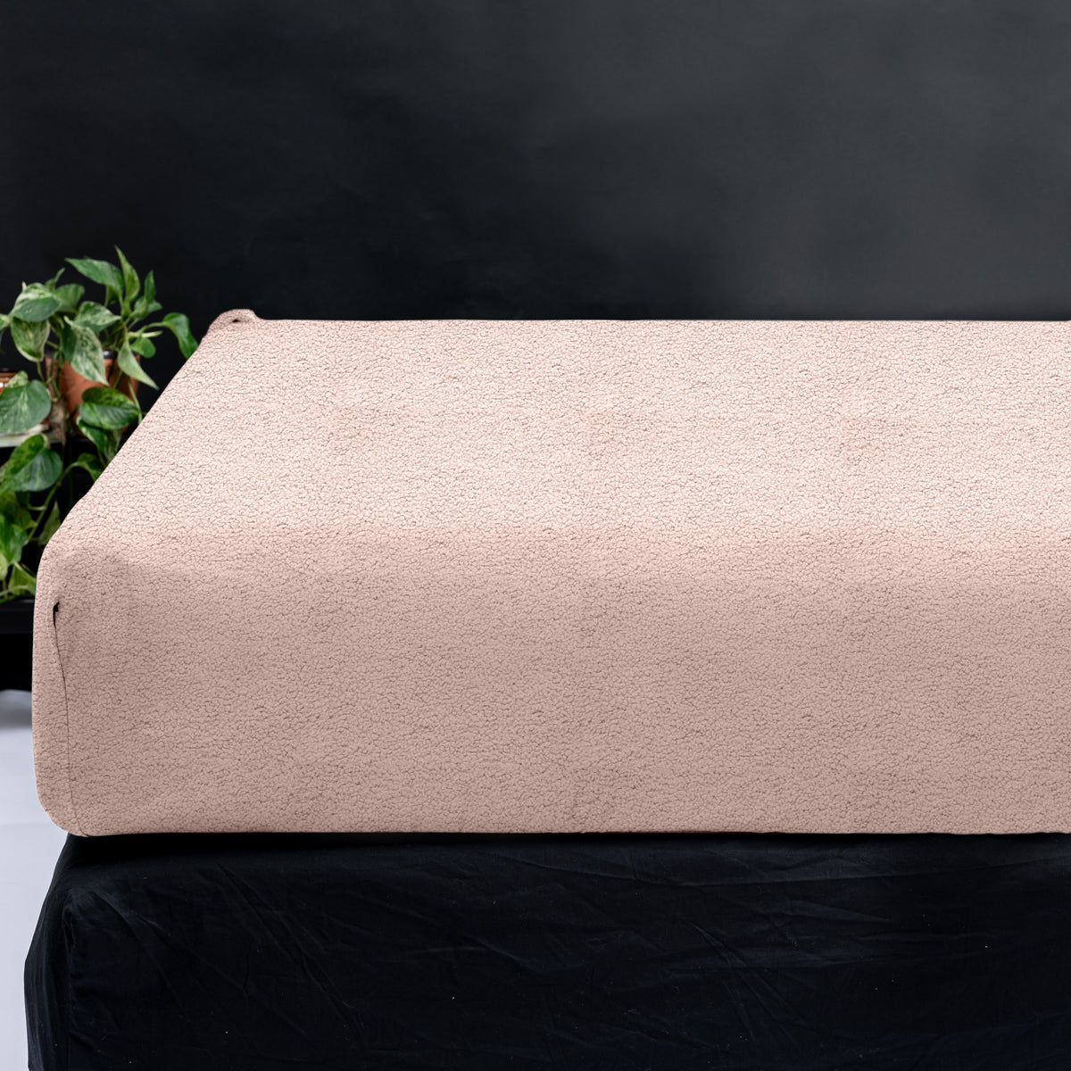 Roze teddy hoeslaken om een matras, met een groene plant en donkere achtergrond