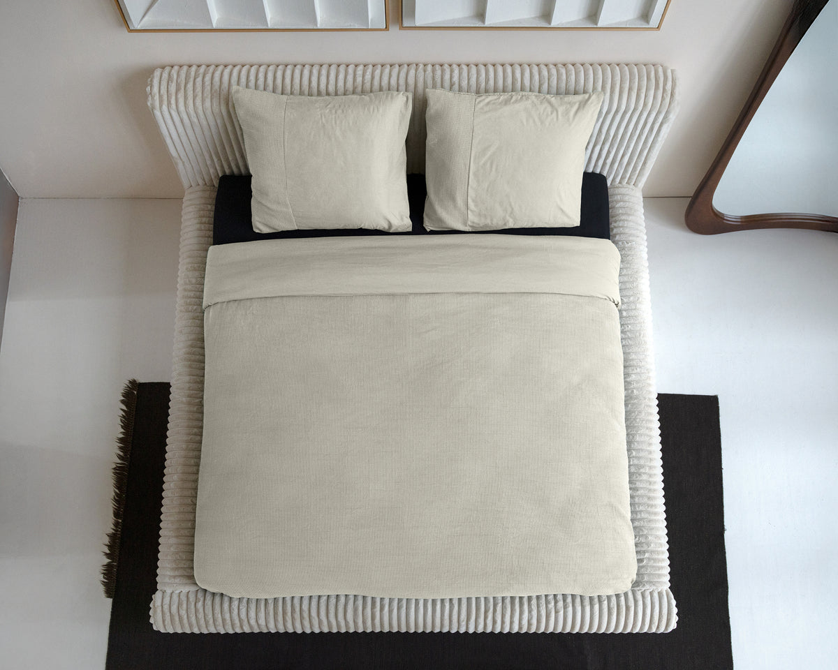 Beige dekbedovertrek met wafelstructuur en twee kussens op een bed, gezien van boven