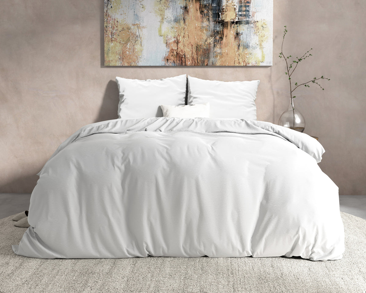 Wit dekbedovertrek met witte kussens op een bed voor een beige muur met schilderij