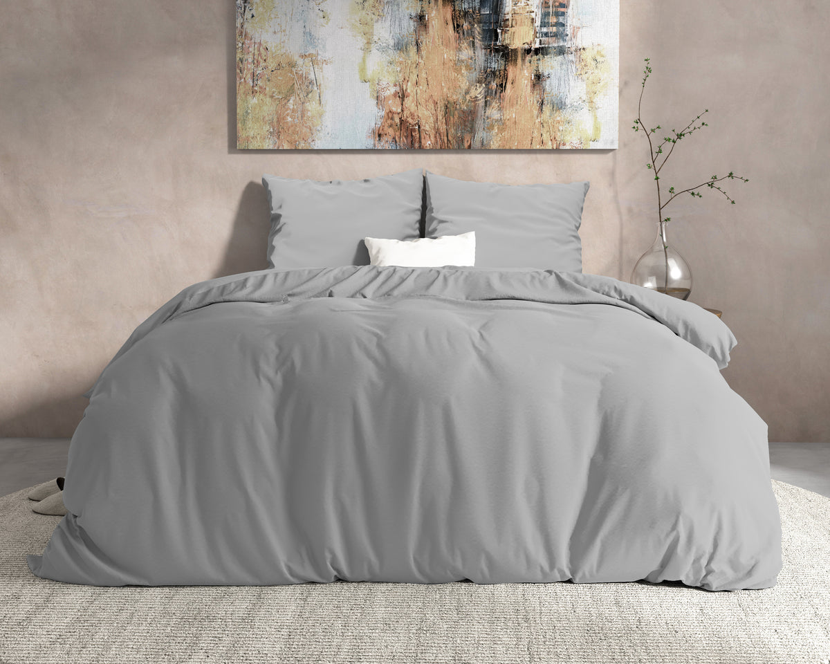 Grijs flanellen dekbedovertrek met twee kussens op een opgemaakt bed voor een beige muur met schilderij