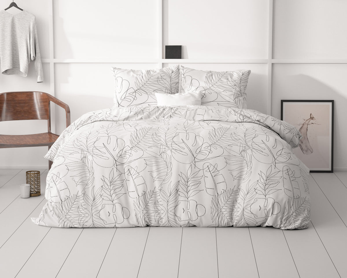 Dekbedovertrek met zwarte lijntekening van bladeren en kussens op een bed in een lichte slaapkamer