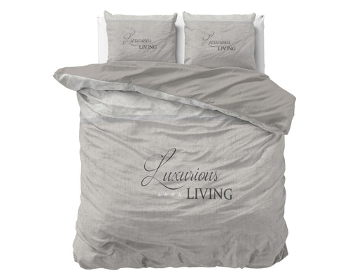 Dekbedovertrek in zand met de tekst Luxurious Living en twee bijpassende kussenslopen op een bed