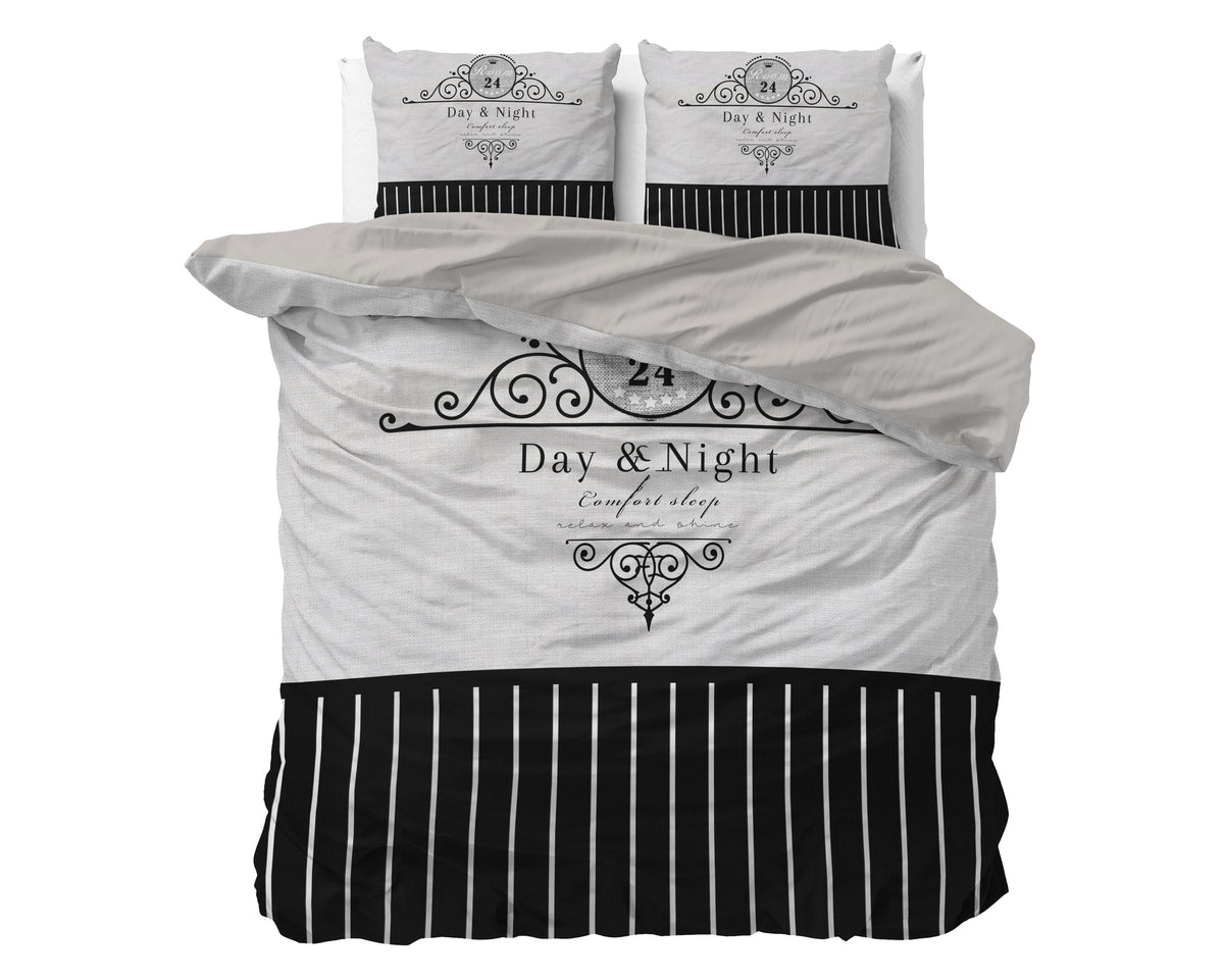 Zwart-grijs dekbedovertrek met sierlijke print, tekst Day & Night en witte streepjes, met twee kussenslopen op een bed