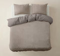 Taupe dekbedovertrek met tint-op-tint motief en donkere effen achterkant, met twee kussens op een bed, gezien van boven