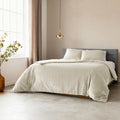 Bed opgemaakt met beige velvet dekbedovertrek en twee kussens, voor een grijs hoofdbord en beige muur