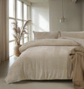 Bed met taupe teddy dekbedovertrek met visgraatpatroon in een lichte slaapkamer met pampasgras en hanglamp