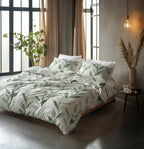 Bed met wit dekbedovertrek met groene bladerenprint en bijpassende kussens in een slaapkamer met grote ramen