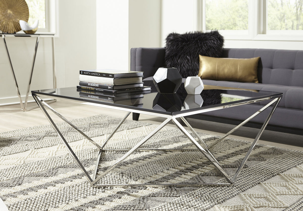 Vierkante salontafel met zwart glazen blad en glanzend metalen geometrisch onderstel in een woonkamer met grijze bank