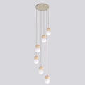 Hanglamp met beige ronde plafondplaat en zes snoeren met houten bollen en witte glazen kappen op verschillende hoogtes