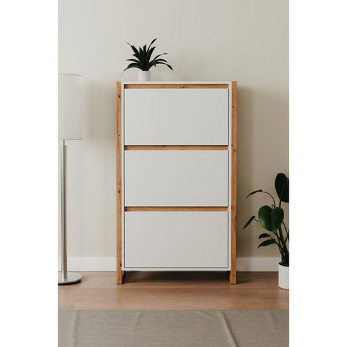 Witte schoenenkast met eikenkleurige rand en drie fronten, naast een staande lamp en planten