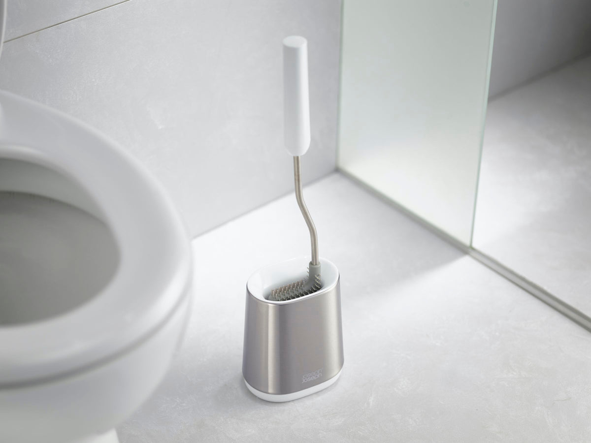 Toiletborstel met wit handvat en flexibele kop in een zilverkleurige houder naast een wit toilet