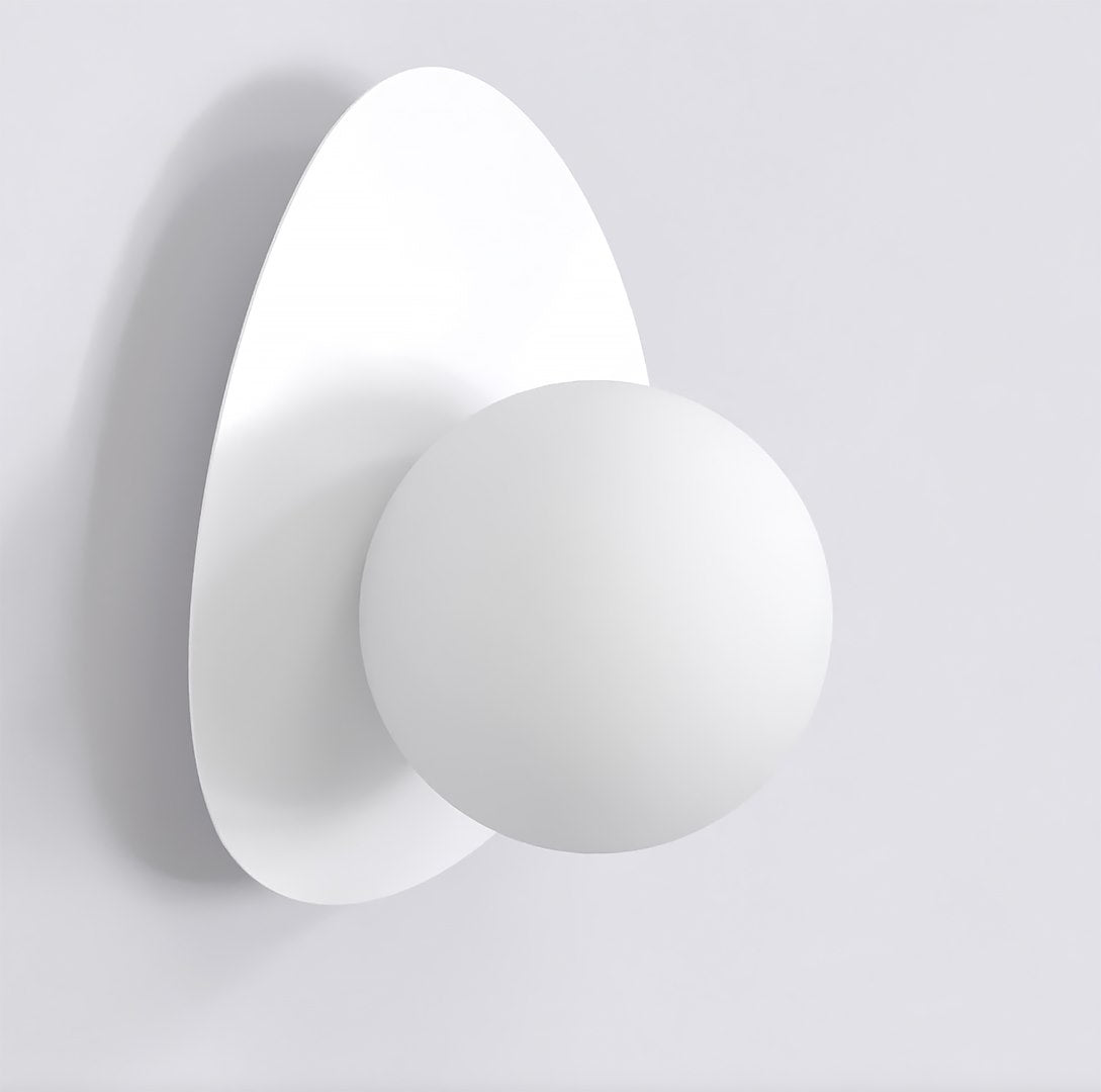 Witte wandlamp met ronde bol op een keivormige witte achterplaat tegen een lichte muur