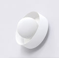Witte wandlamp met matte bolkap in een gedraaide, ronde band tegen een lichte muur