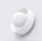 Witte wandlamp met matte bolkap in een gedraaide, ronde band tegen een lichte muur