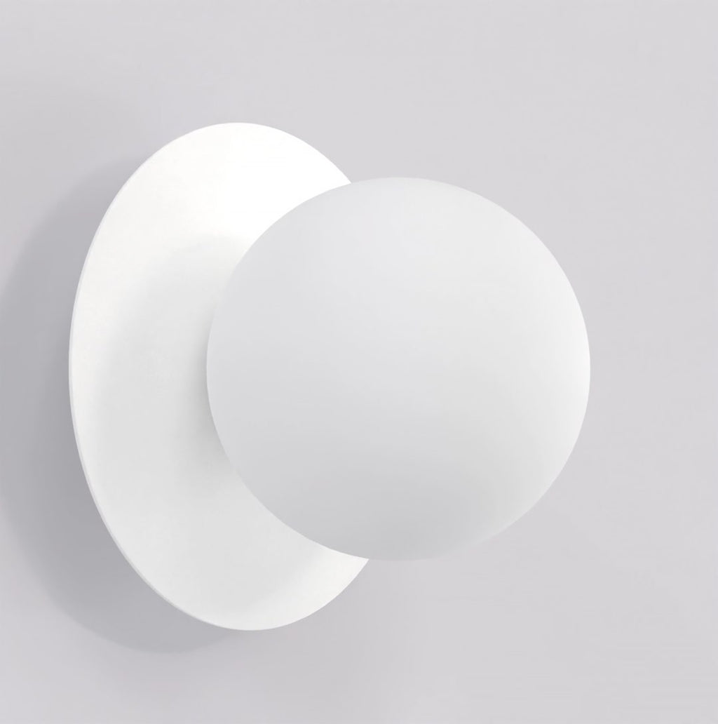 Witte wandlamp met matte ronde bol voor een ronde witte achterplaat tegen een lichte wand