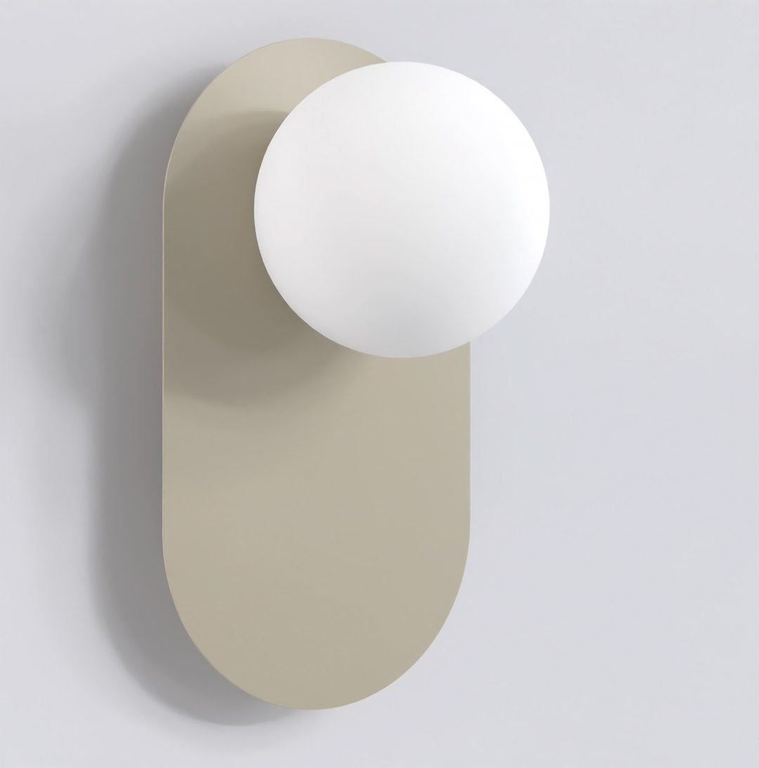Wandlamp met matte witte bol op een langwerpige, afgeronde montageplaat in mokka tegen een lichtgrijze wand