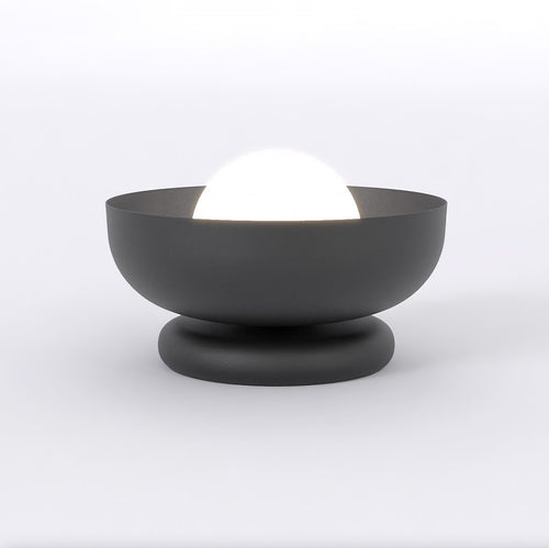 Zwarte tafellamp met een brede kom op een ronde voet en een verlichte witte glazen bol erin