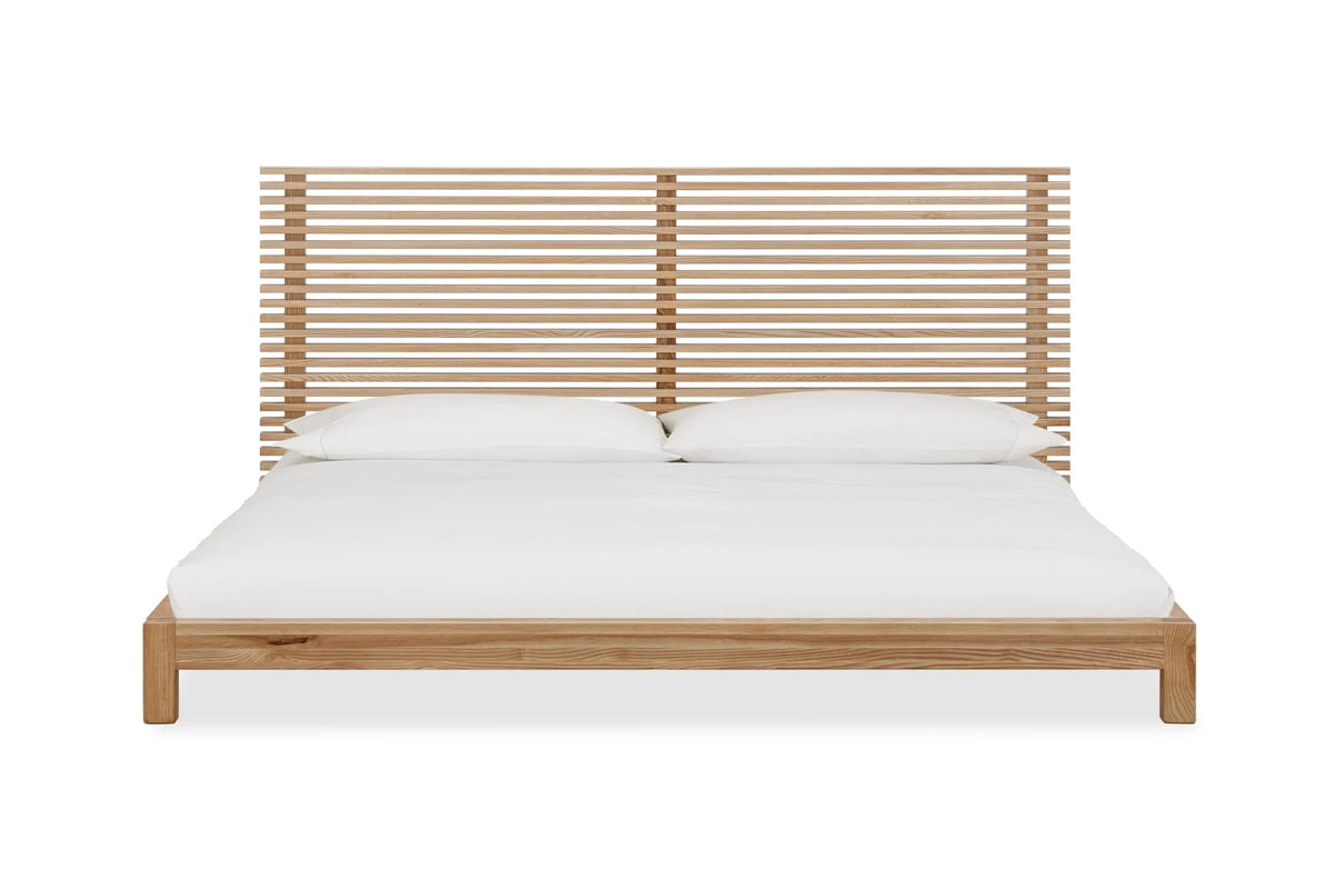 Houten platformbed met slatted hoofdbord van essen, opgemaakt met wit beddengoed en twee witte kussens